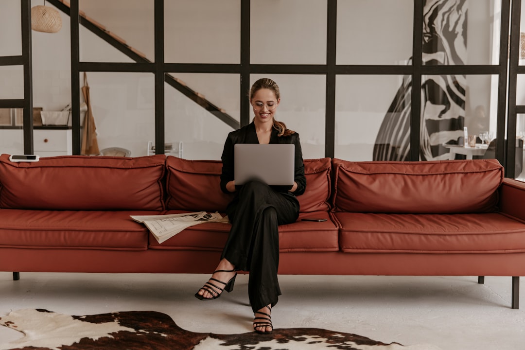 A woman relaxes on a stylish sofa in a minimalist living room, browsing a home furnishings website on her tablet.