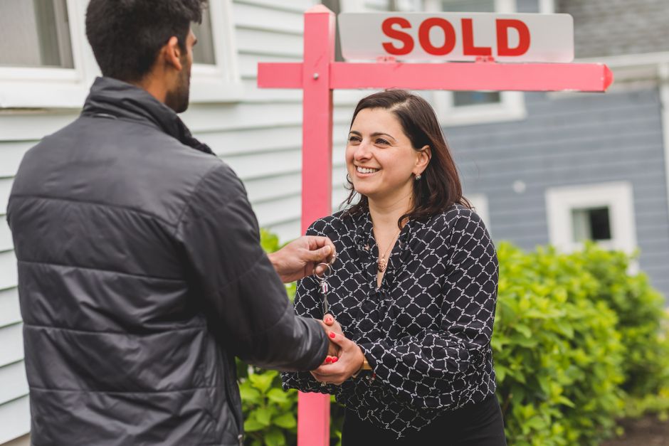 A professional real estate agent shakes hands with a happy couple in front of a beautiful modern home, finalizing the sale.